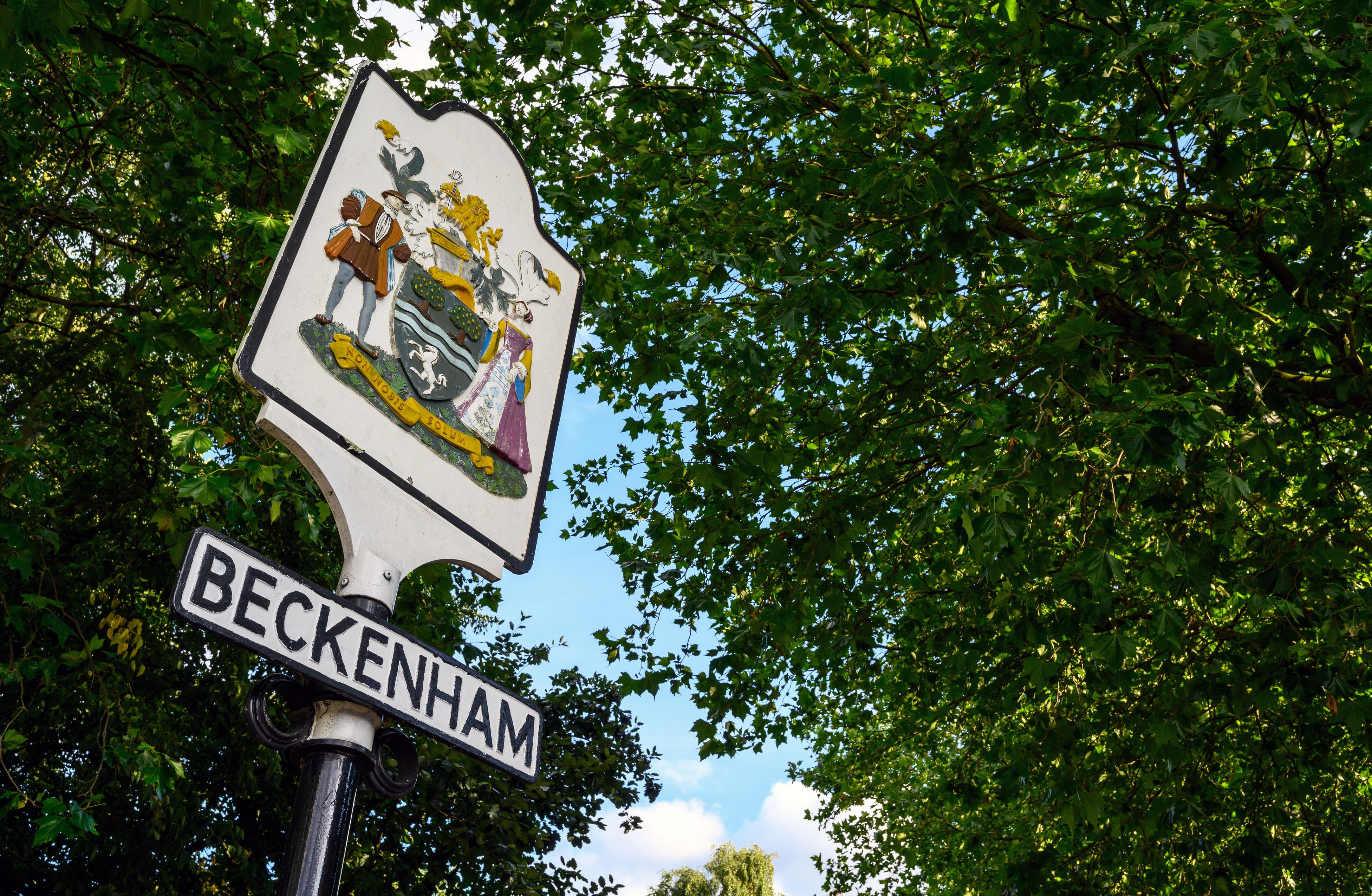 Traditional Beckenham town sign surrounded by lush green trees, set against a bright blue sky. The sign, featuring a colourful historic crest, is a well-known local landmark and symbol of community pride. This image captures the character of Beckenham, combining heritage with a welcoming atmosphere, making it a highly sought-after place to live in South East London.