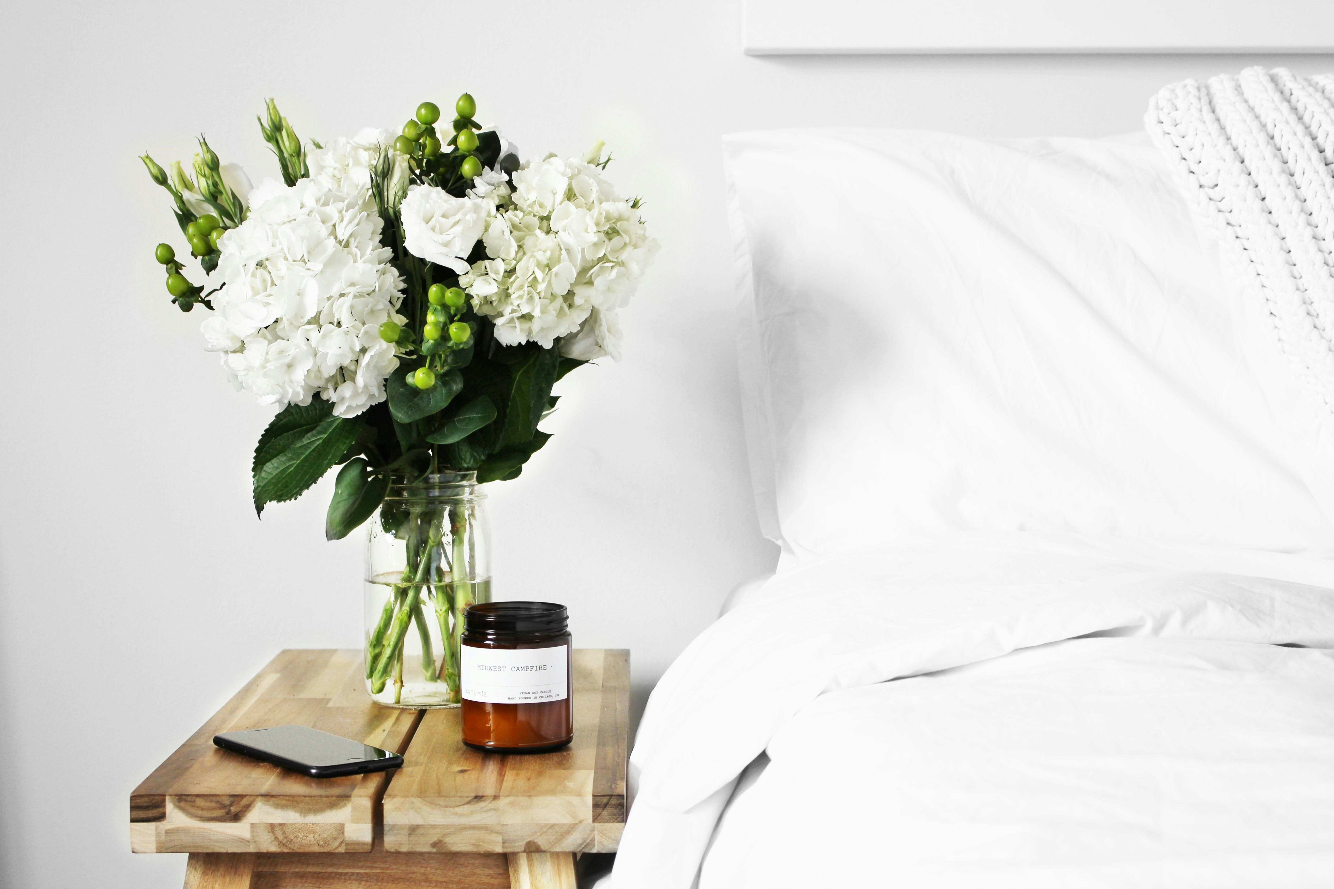A minimalist, calming bedroom scene featuring a glass jar of fresh white flowers and a softly scented candle, perfectly showcasing how fragrance and floral touches elevate the appeal of a home. When preparing properties for sale in Beckenham, Orpington, Catford, Bromley, and across South East London, Integra Estates encourages sellers to embrace simple but effective staging techniques. The right scent and a clean, fresh aesthetic can help buyers instantly connect with a space, making it feel more like home.