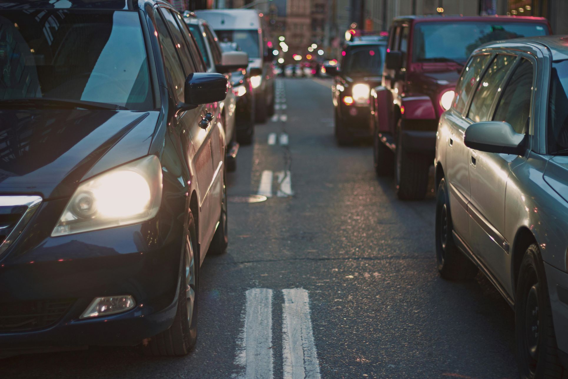 Close-up view of cars stuck in heavy traffic on an urban road during the evening rush hour. The scene captures headlights shining, vehicles lined up, and the congested flow of city life. Ideal for illustrating topics such as commuting, congestion, urban planning, transport issues, or property market trends related to road access and travel times in areas like South East London and North Kent.