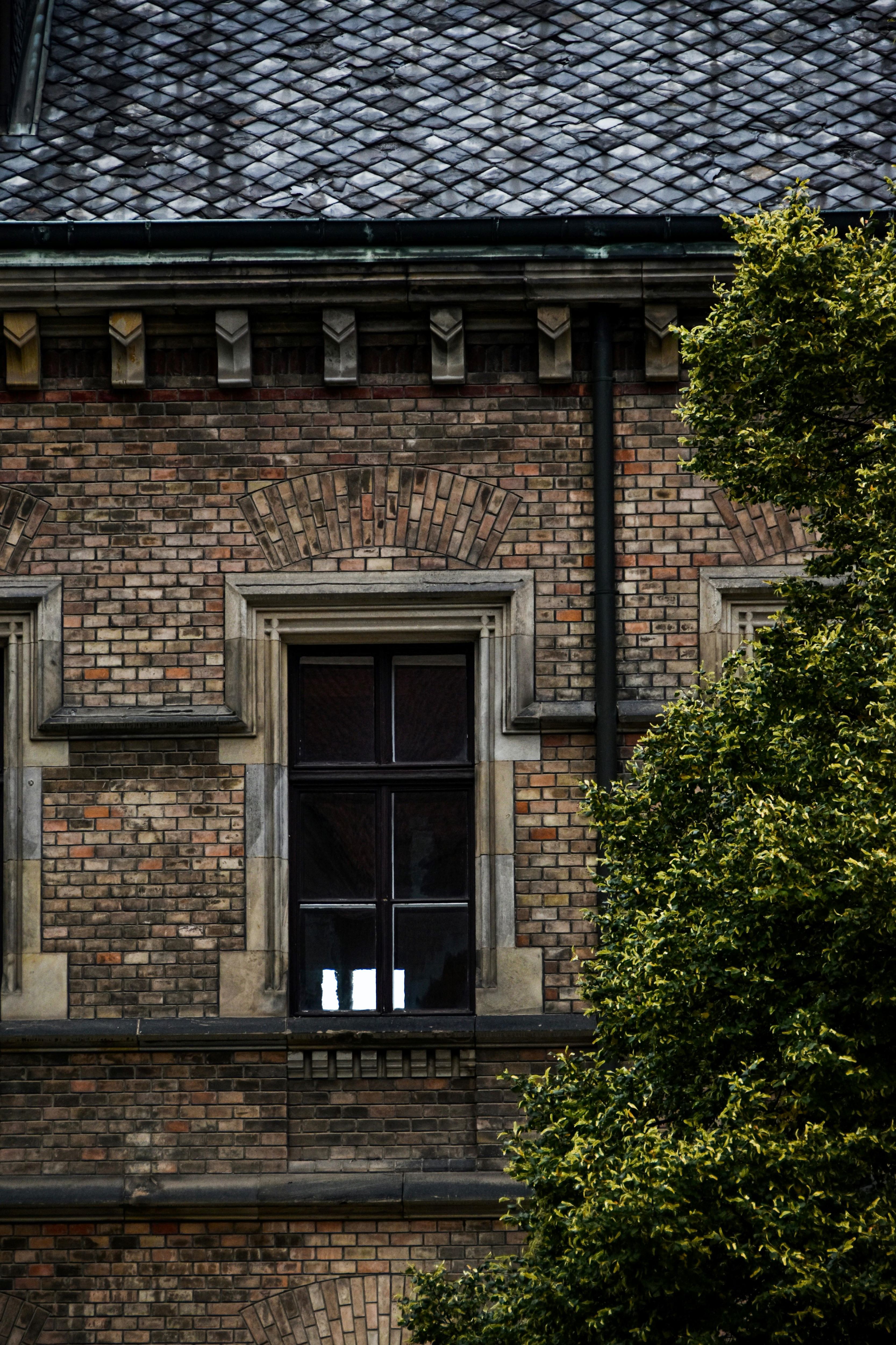 Close-up view of a traditional brick building facade with detailed masonry, arched stonework above windows, and a classic slate roof. The image captures the elegance of period architecture often found in Beckenham, Orpington, and Penge. Estate agents in these areas frequently highlight such heritage details to attract buyers who value character homes, timeless craftsmanship, and historical charm