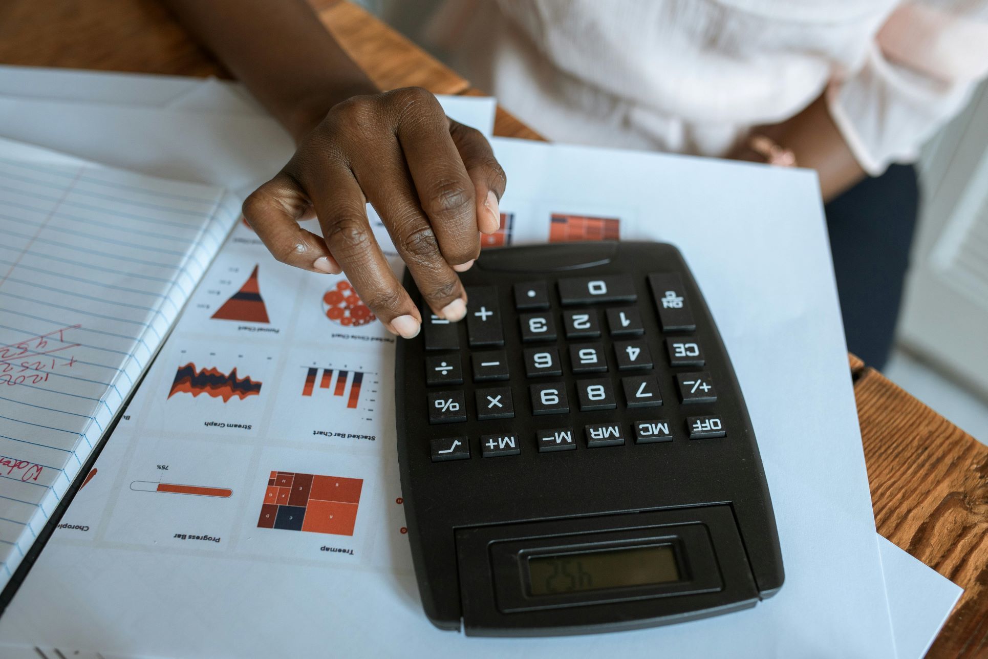 Close-up of a person using a calculator for property valuation alongside financial charts. Integra Estates provides expert home valuations, sales, and advice for anyone searching ‘estate agents Beckenham’, ‘local estate agents in Beckenham’, or the ‘nearest estate agent to me in Beckenham
